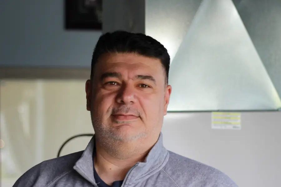 Headshot of Arsen Oganesyan, Warehouse and Fleet Manager, smiling in an office with HVAC equipment visible in the blurred background.