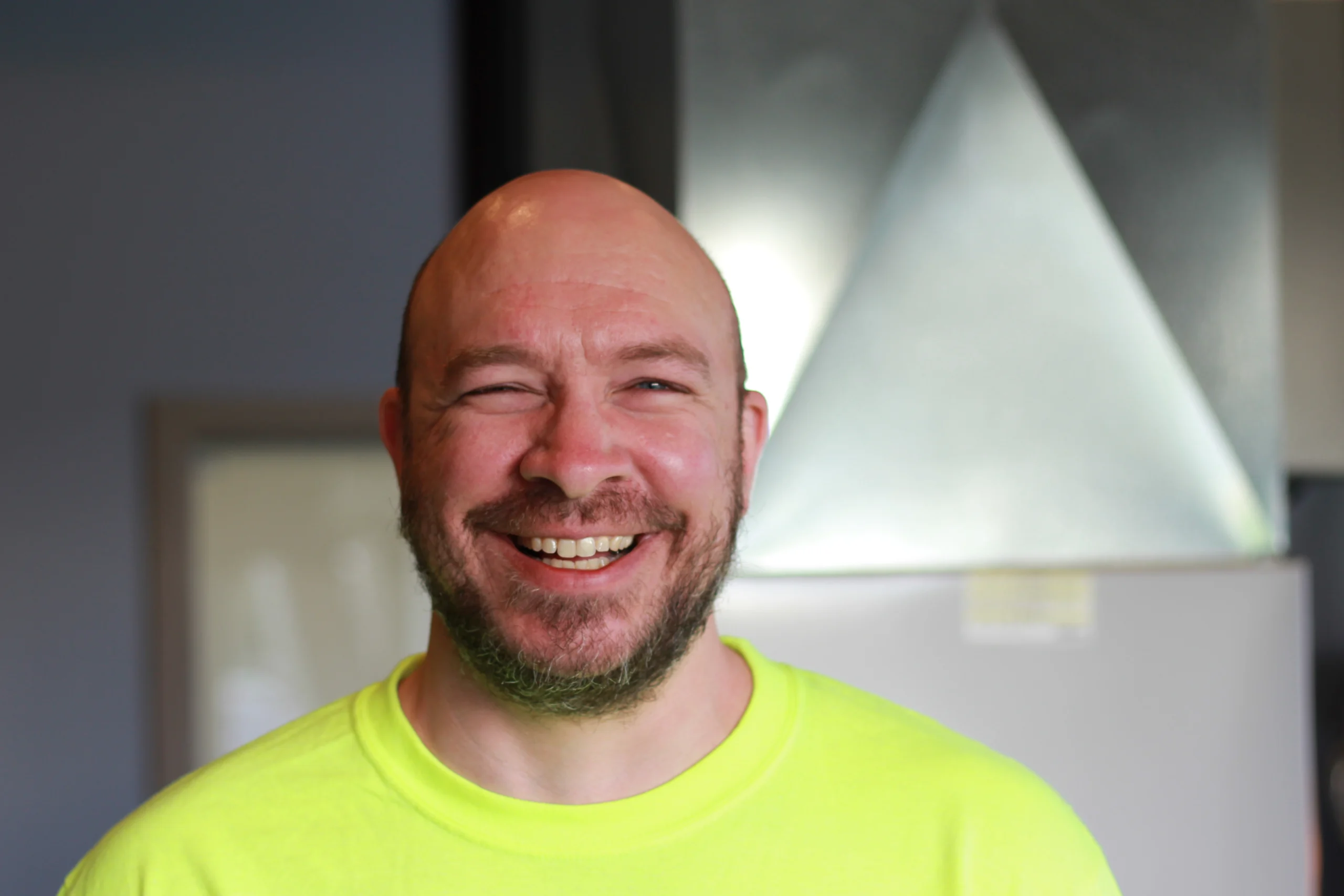 Cory Rauckman, K Komfort HVAC Technician A professional headshot of Cory Rauckman, an EPA-certified HVAC service technician at K Komfort, laughing happily in front of an indoor sheet metal ventilation system.