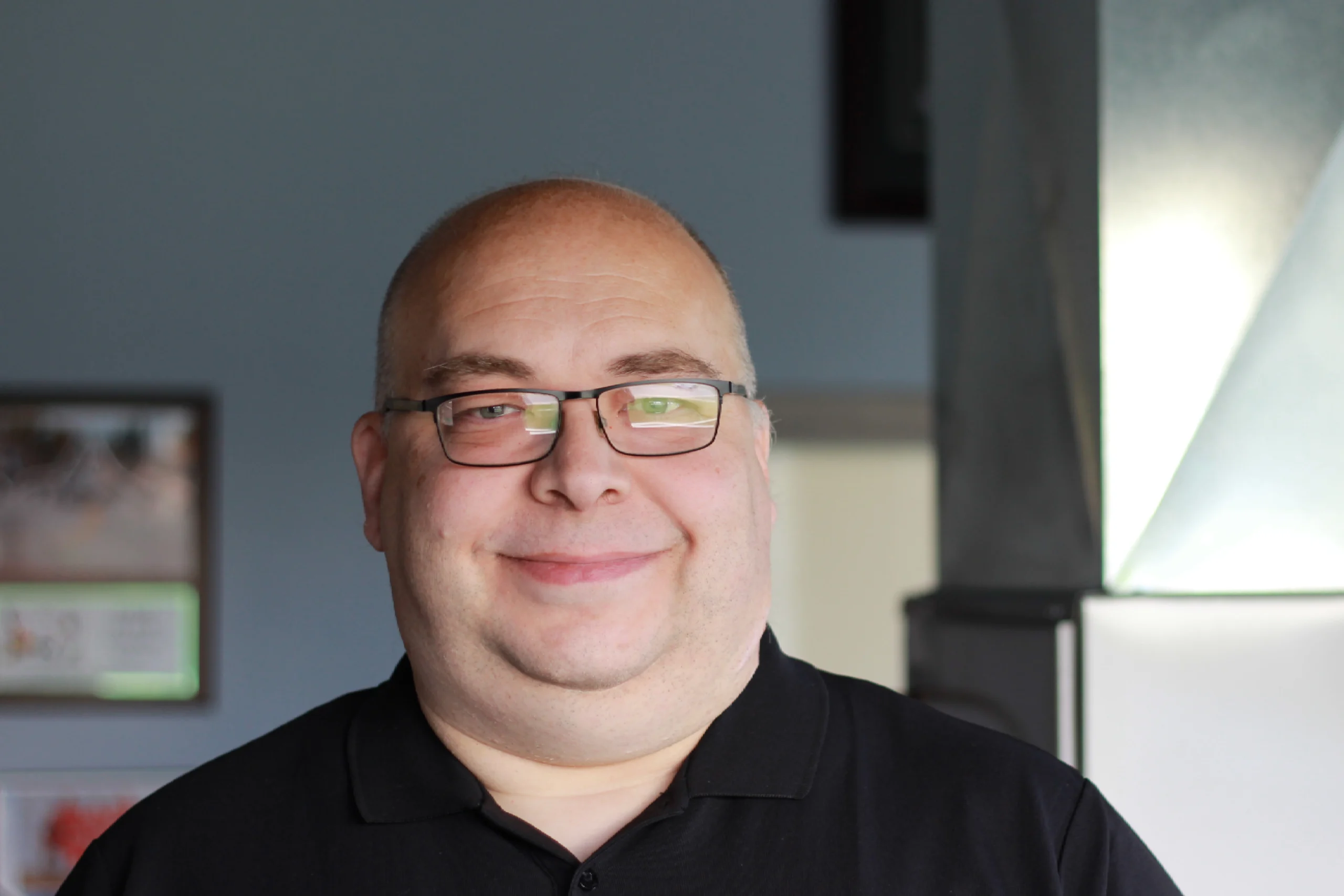 Michael Buehl, K Komfort Senior HVAC Designer A professional headshot of Michael Buehl, the Senior HVAC Designer at K Komfort, smiling in front of a blurred metallic sheet metal ductwork installation.