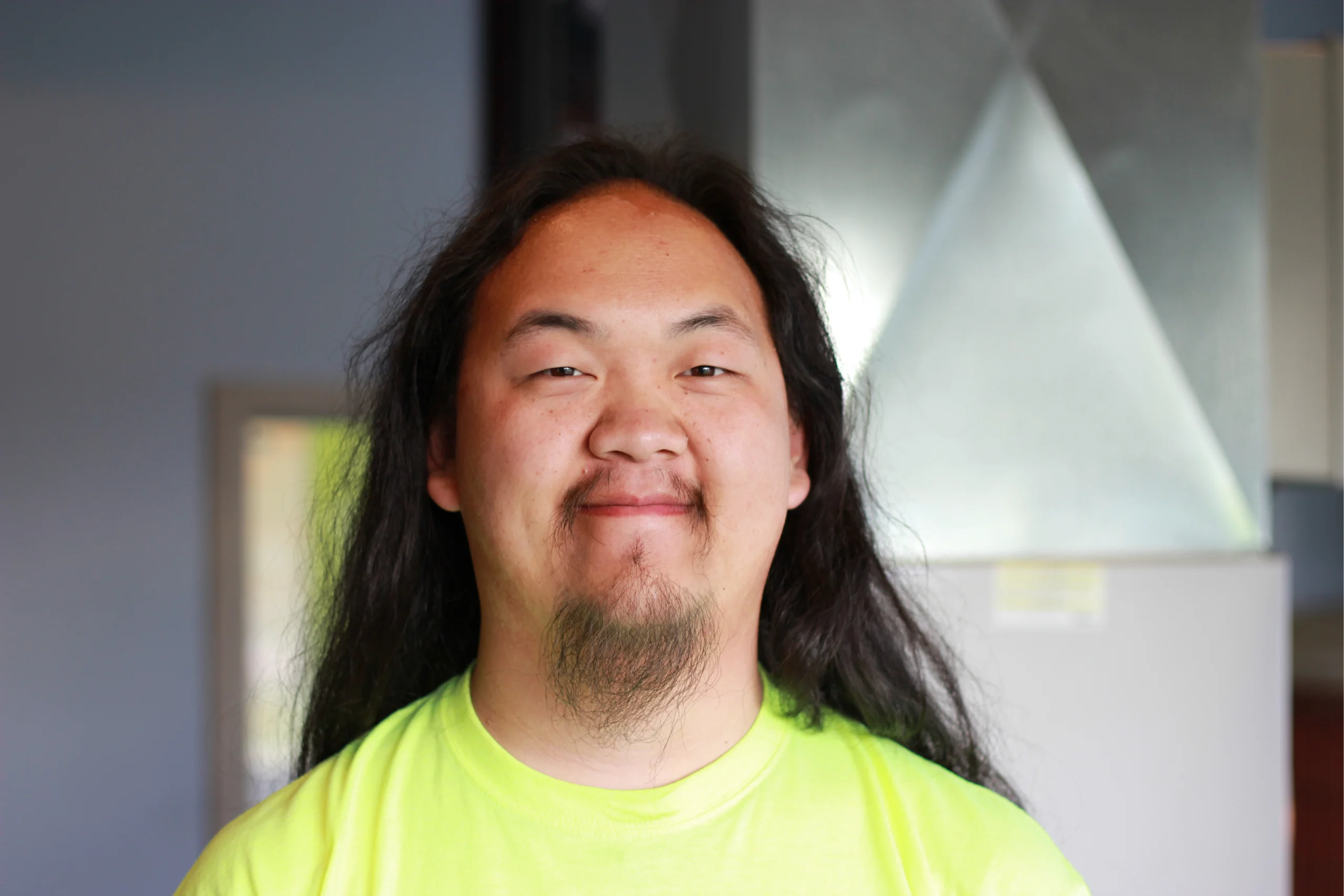 Ryu Xiong, K Komfort HVAC Technician A professional headshot of Ryu Xiong, a technical-diploma-certified HVAC service technician at K Komfort, smiling in front of an indoor heating and cooling system.