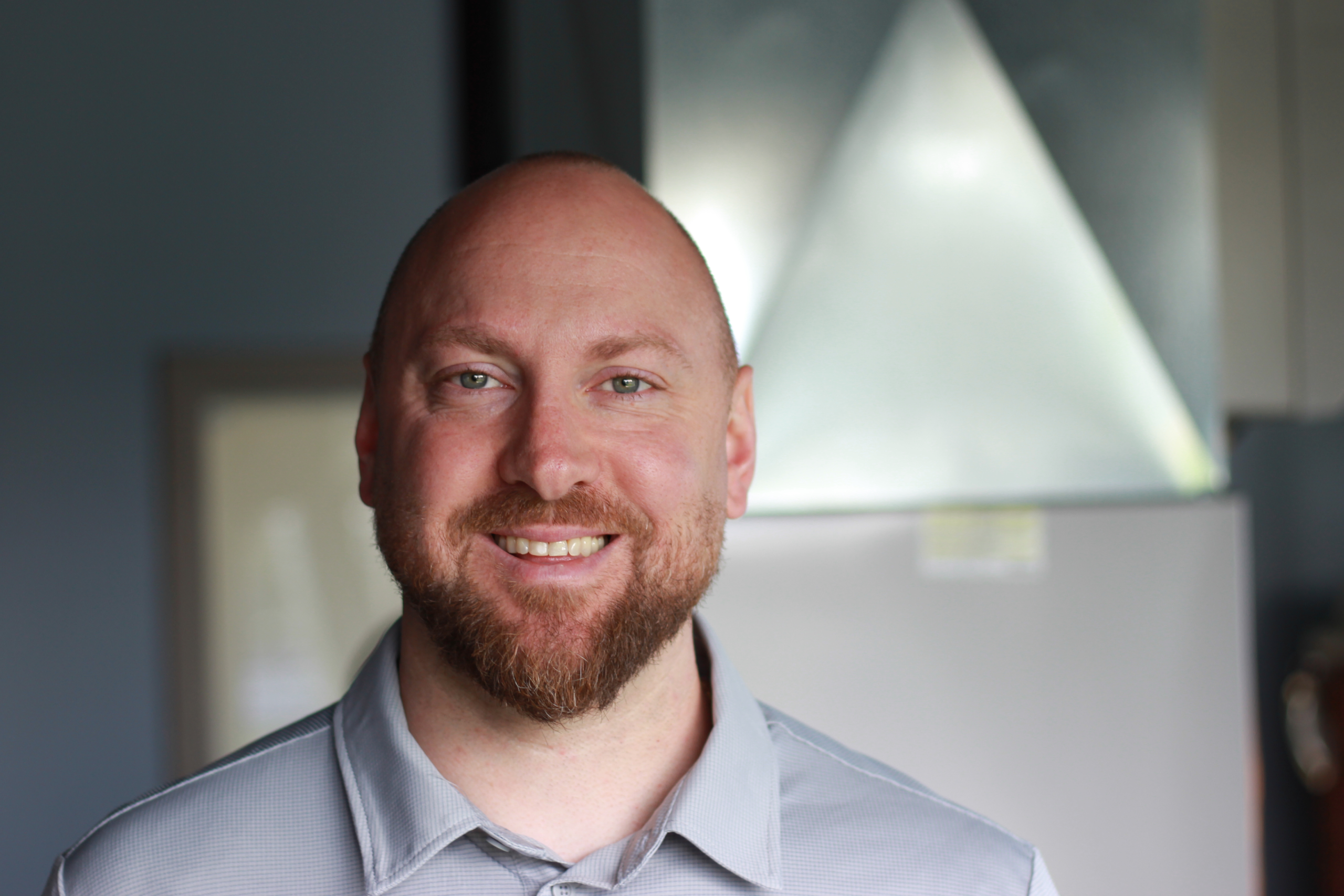 Shawn Lonardelli, K Komfort Senior Project Manager A professional headshot of Shawn Lonardelli, Senior Project Manager at K Komfort, smiling in front of a blurred metallic sheet metal installation.