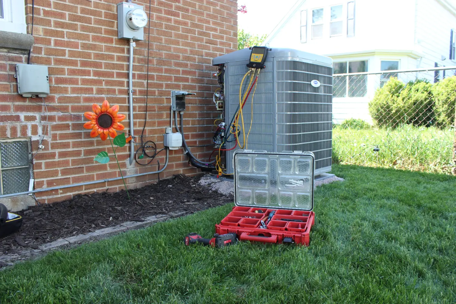 Emergency AC Repair and Maintenance Services Carrier central air conditioning system undergoing maintenance with digital manifold gauges and technician tools in a residential backyard by K Komfort.