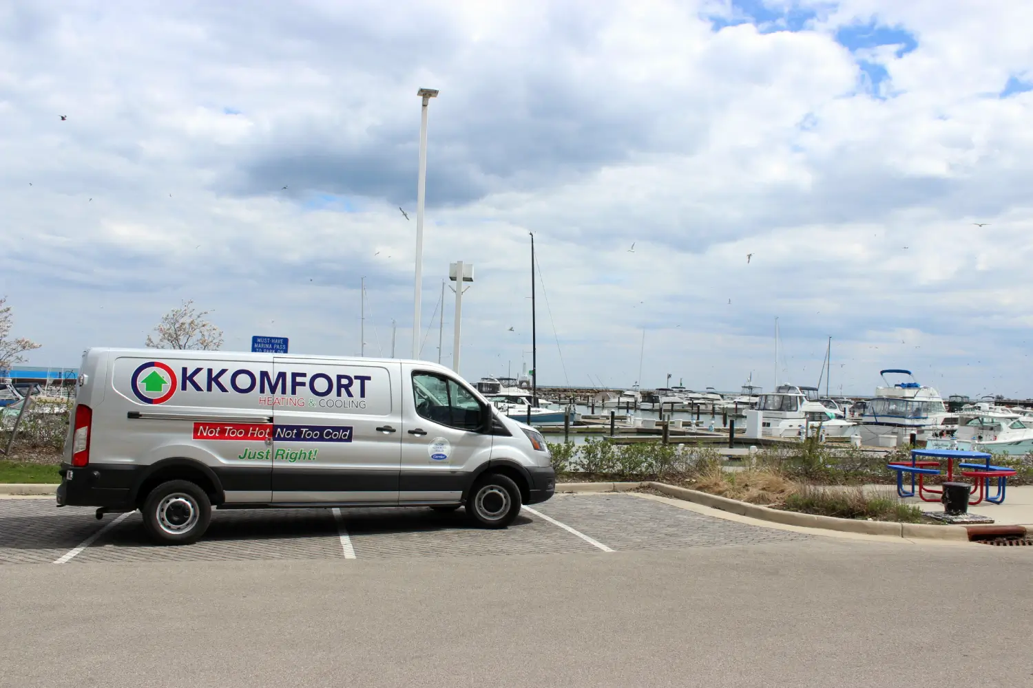 K Komfort Emergency HVAC Service at Port Washington A silver K Komfort Heating & Cooling service van parked in a brick paved stall at the Port Washington Marina boat slips under a cloudy sky in Port Washington, Wisconsin.