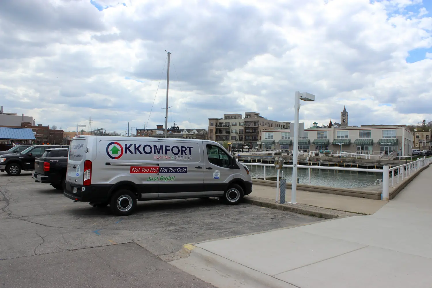 K Komfort HVAC Service Van at Port Washington Marina A silver K Komfort Heating & Cooling service van parked at the Port Washington Marina along the water with the historic St. Mary's Church steeple on the hillside background in Port Washington, Wisconsin.
