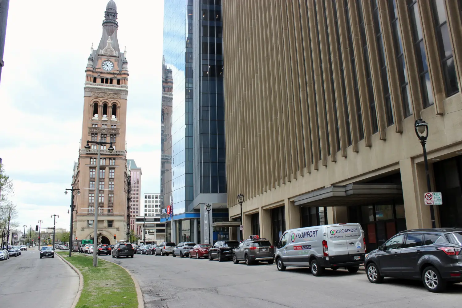 K Komfort Emergency HVAC Service in Downtown Milwaukee A silver K Komfort Heating & Cooling service van parked on North Water Street in downtown Milwaukee, Wisconsin, with the historic Milwaukee City Hall tower and the modern glass BMO Tower in the background.
