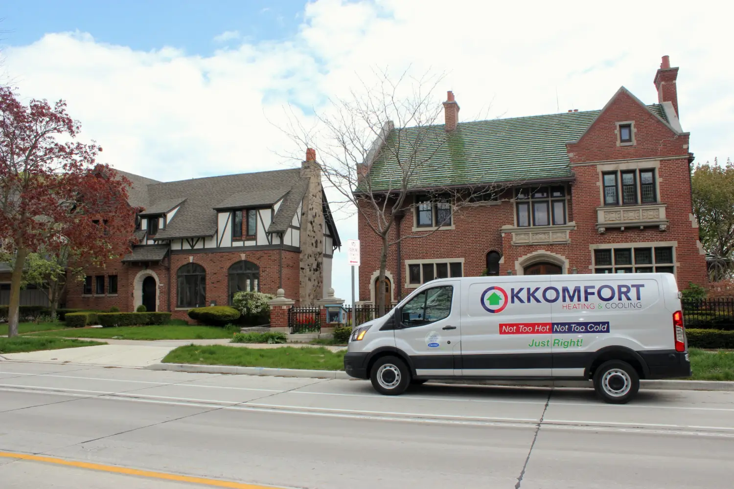 K Komfort Historic Tudor HVAC Service in Whitefish Bay A silver K Komfort Heating & Cooling service van parked on a street in front of two side-by-side historic brick Tudor Revival homes in Whitefish Bay, Wisconsin.