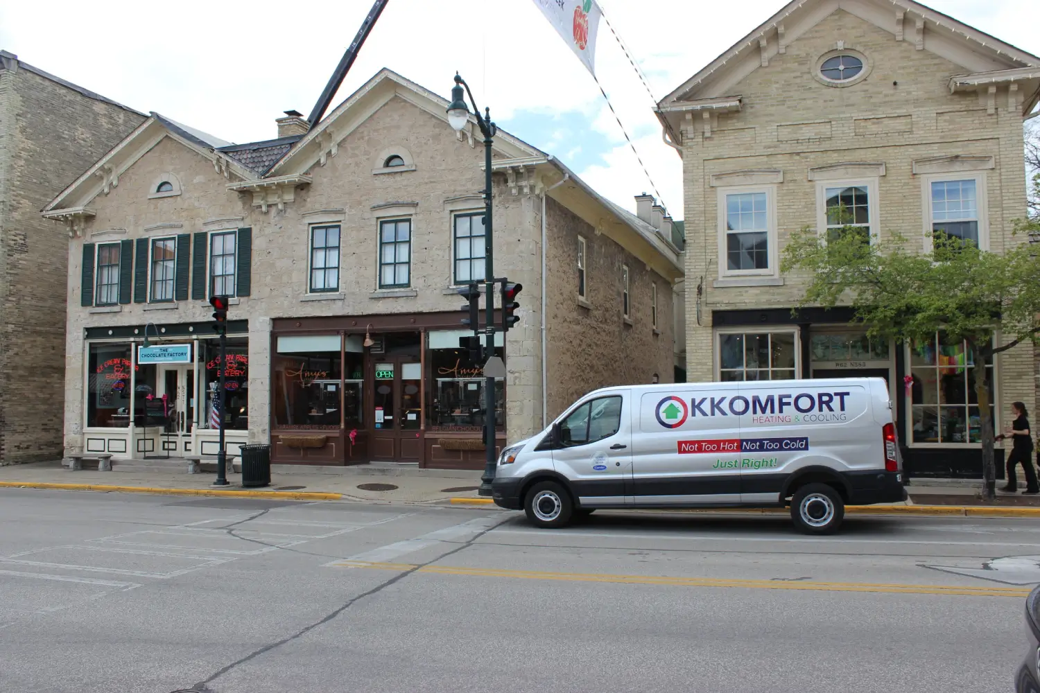 K Komfort Service Van in Downtown Cedarburg A silver K Komfort Heating & Cooling service van parked along the street in downtown Cedarburg, Wisconsin, in front of Amy's Candy Kitchen and historic stone storefronts on Washington Avenue.