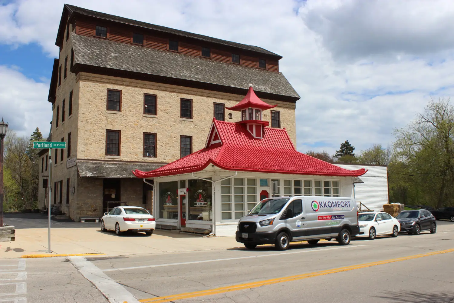 K Komfort HVAC Service at Cedarburg Mill A silver K Komfort Heating & Cooling service van parked along Portland Road next to the historic red-roofed pagoda building and the stone Cedarburg Mill in Cedarburg, Wisconsin.