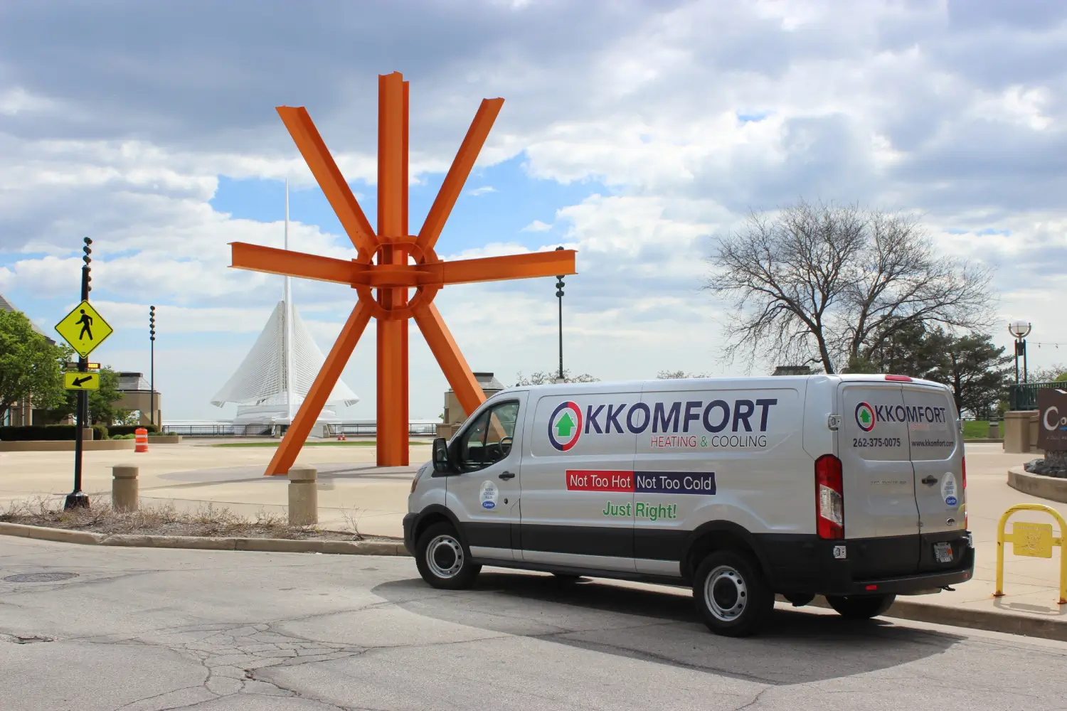 A silver K Komfort Heating & Cooling service van parked near the orange The Calling sculpture with the white Milwaukee Art Museum in the background on the lakefront in Milwaukee, Wisconsin.