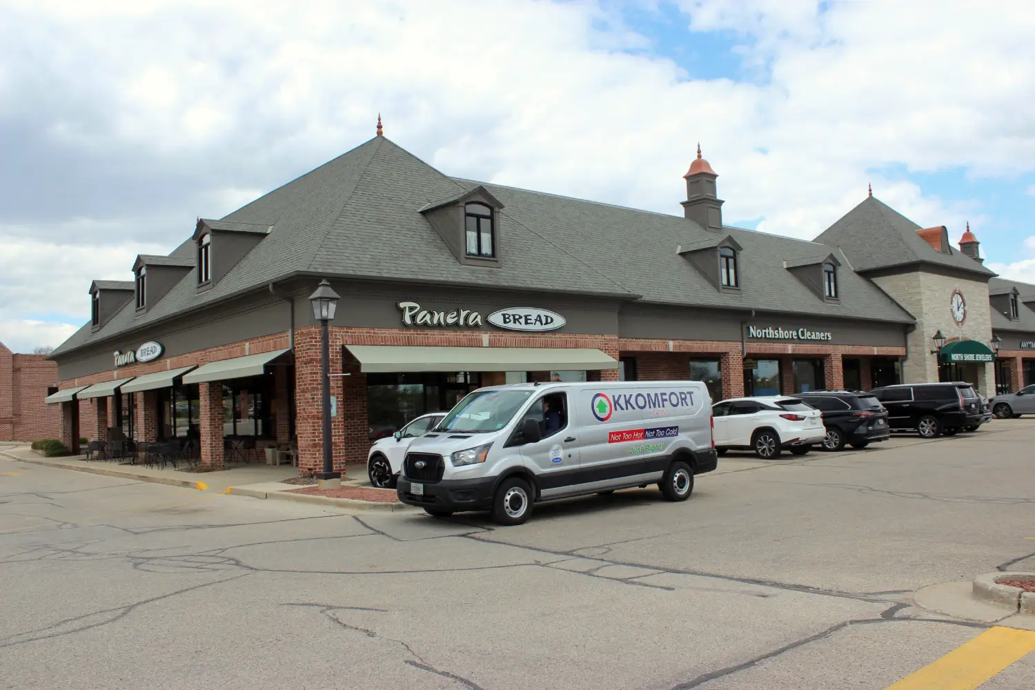 K Komfort HVAC Service on Port Washington Road in Mequon A silver K Komfort Heating & Cooling service van parked in a commercial plaza on Port Washington Road in Mequon, Wisconsin, in front of Panera Bread, Northshore Cleaners, and North Shore Jewelers.