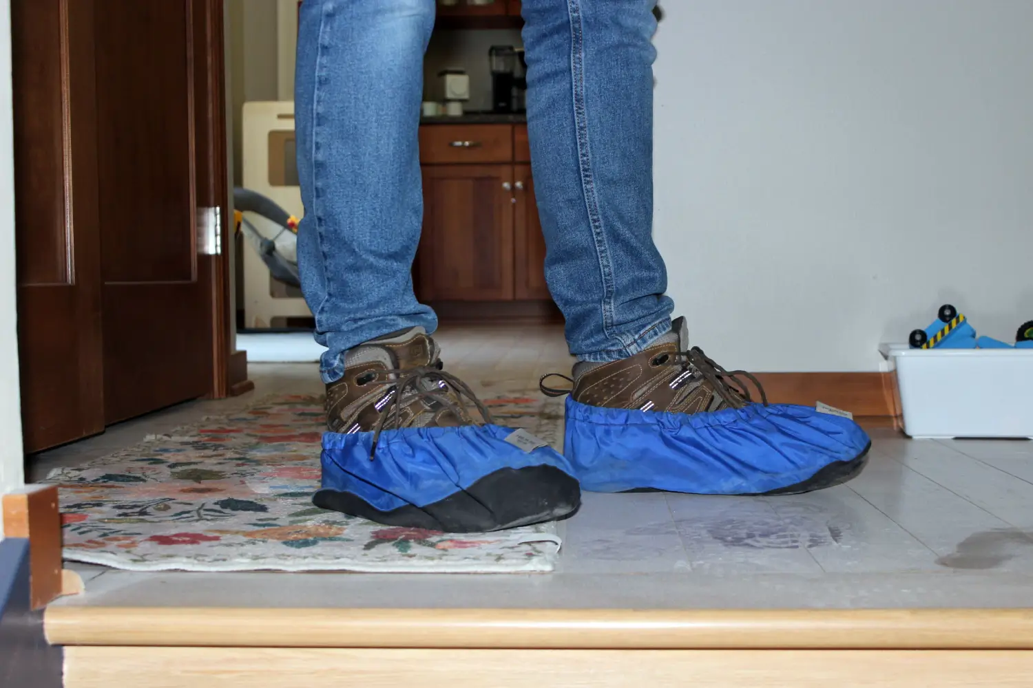 K Komfort Home Property Protection Shoe Covers An HVAC service technician wearing protective blue shoe covers over work boots inside a home entryway to protect floors.