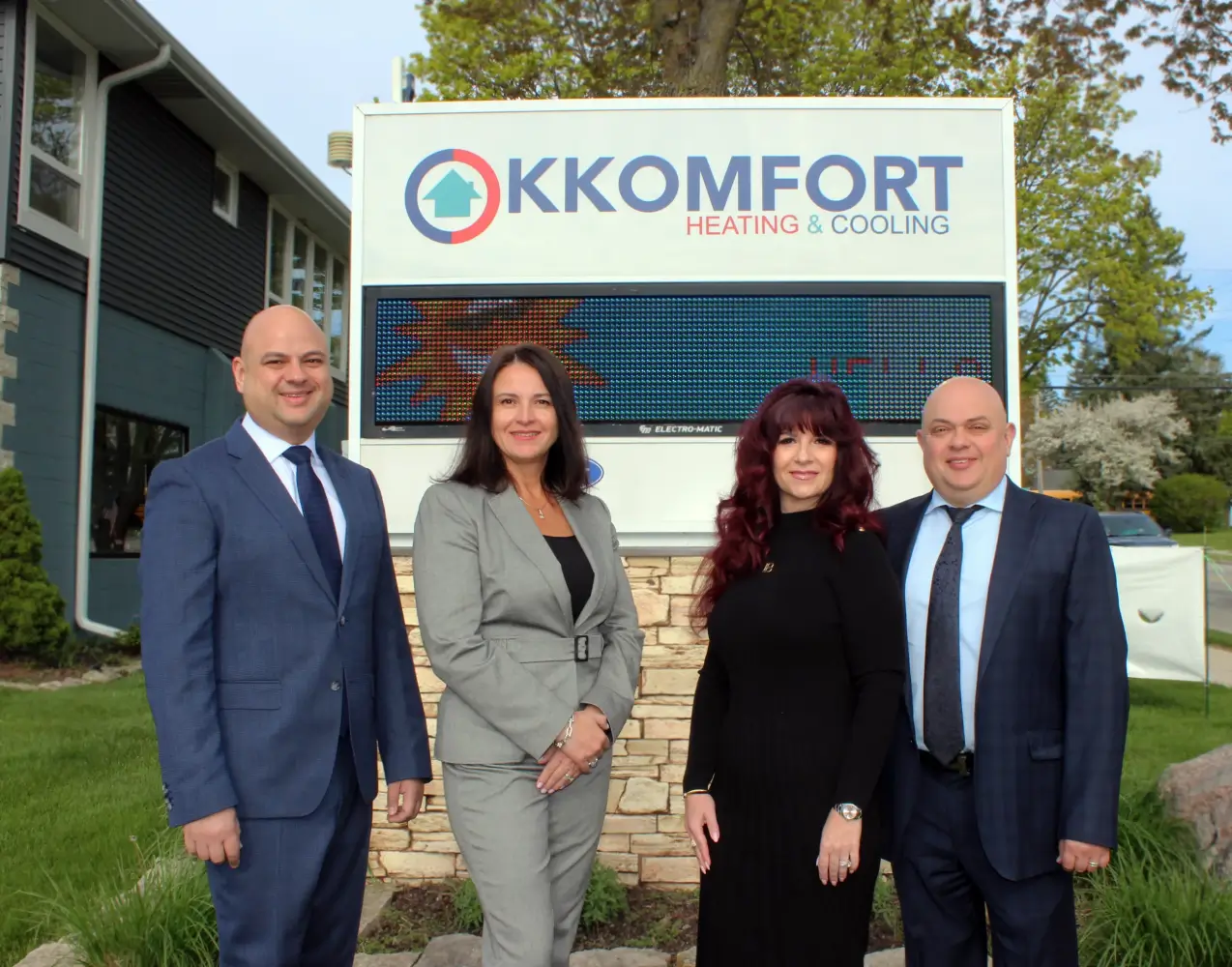 The K Komfort Heating and Cooling leadership team standing together outside their company headquarters sign in Grafton, Wisconsin.