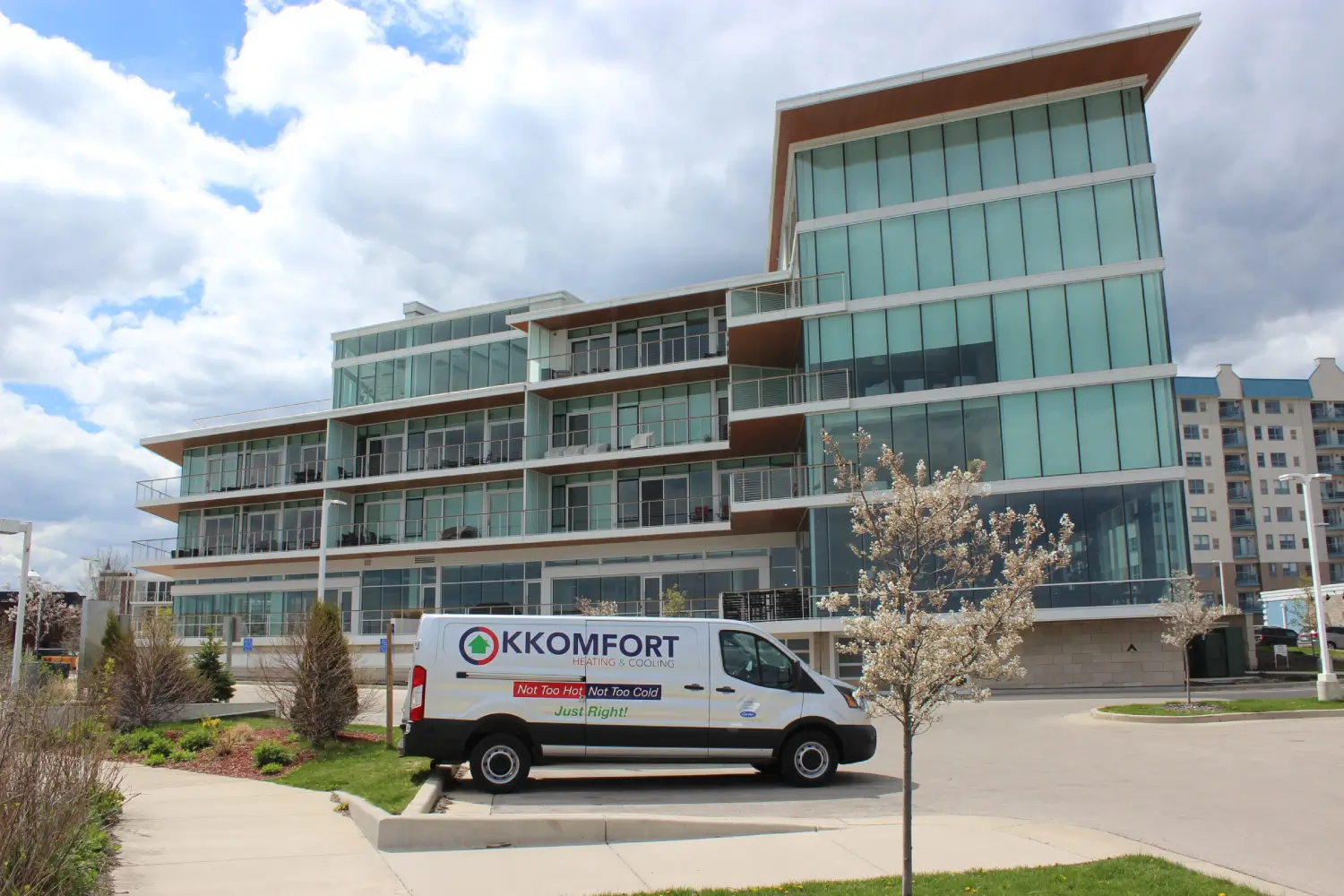 K Komfort HVAC Service at Port Washington Lakefront Condos A silver K Komfort Heating & Cooling service van parked in front of modern glass lakefront condominiums near the marina in Port Washington, Wisconsin.
