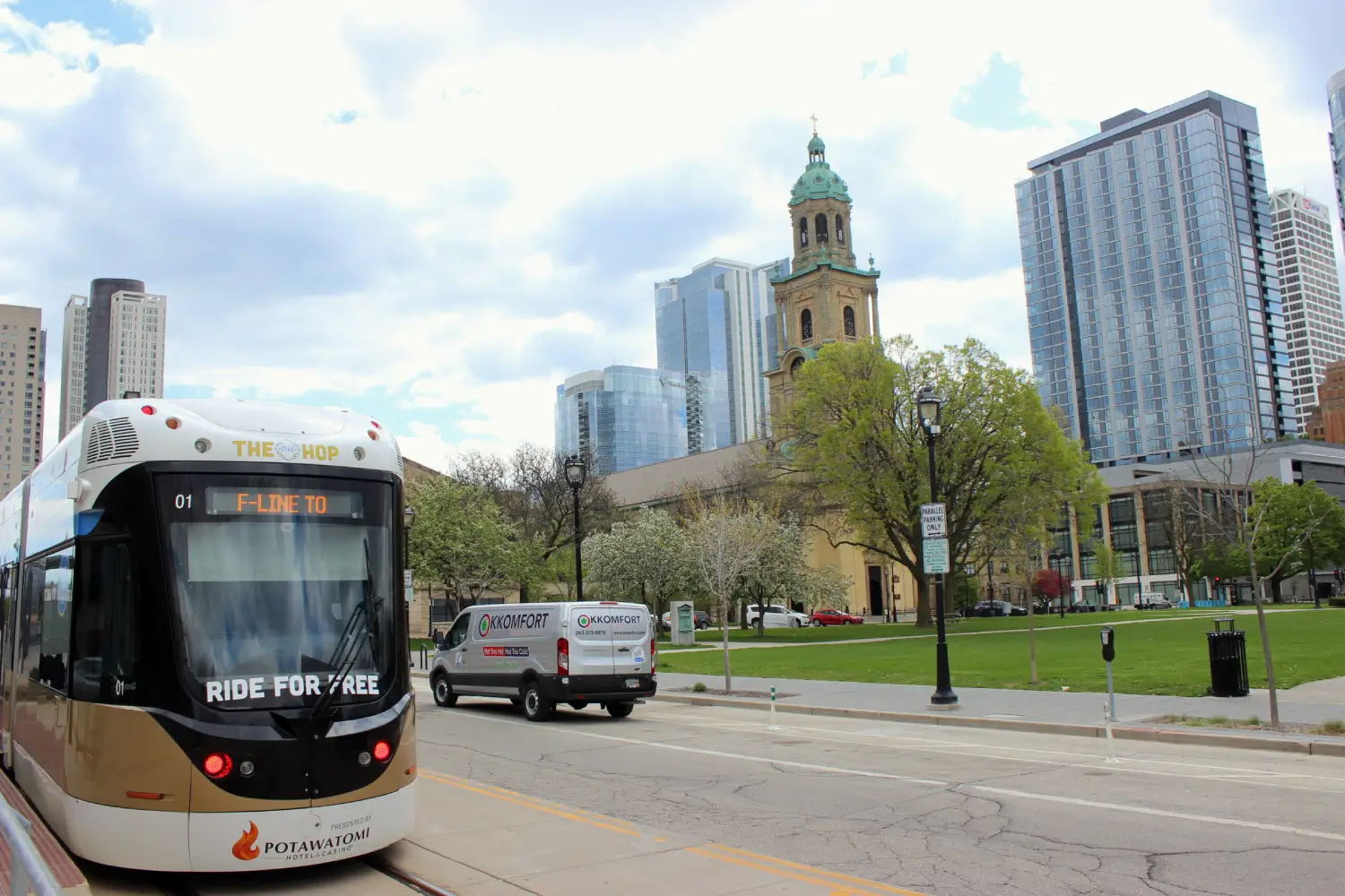 K Komfort HVAC Service Van near Cathedral Square Park A silver K Komfort Heating & Cooling service van driving past The Hop streetcar and Cathedral Square Park with the Cathedral of St. John the Evangelist in downtown Milwaukee, Wisconsin.
