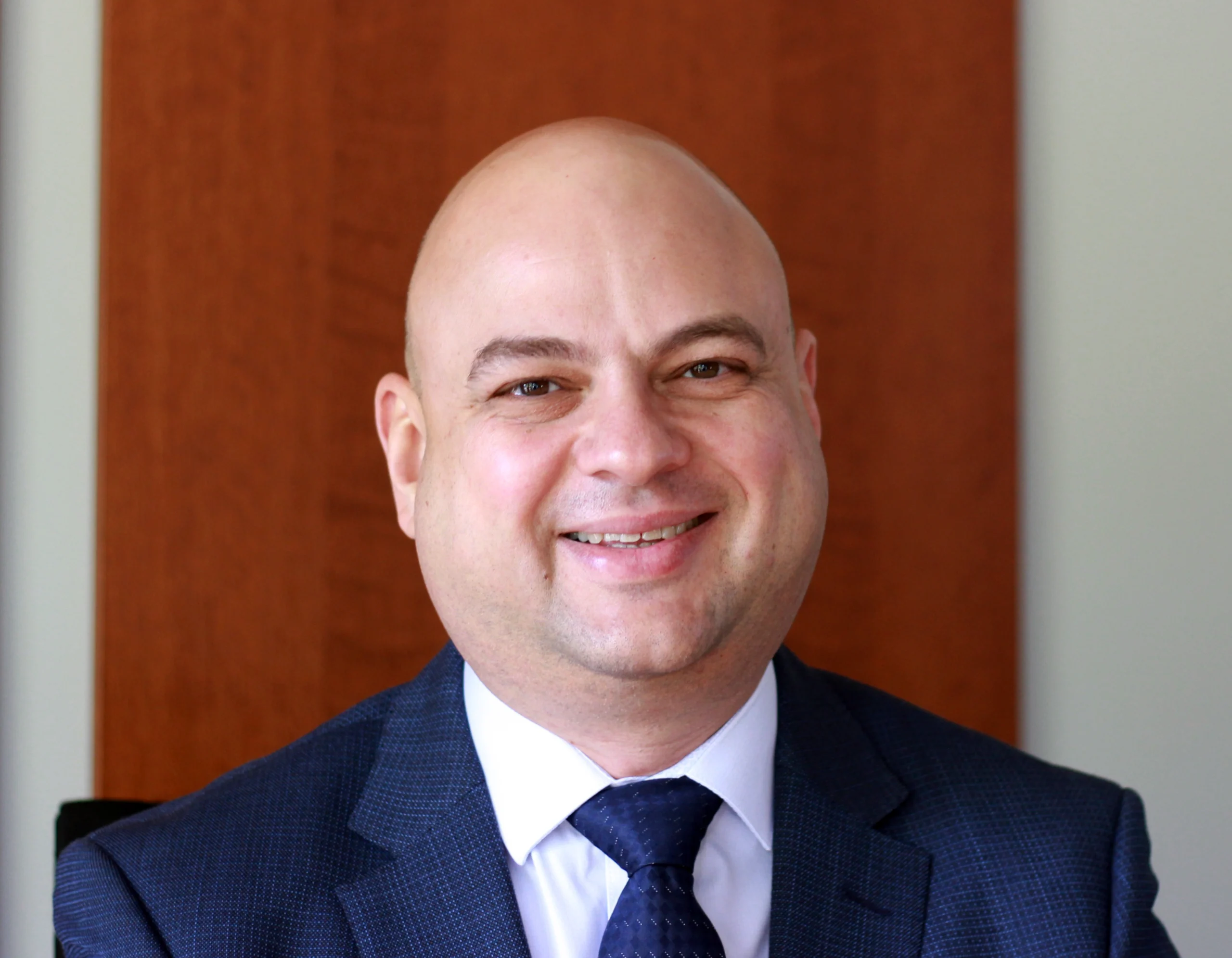 Slava Krol, K Komfort President A professional portrait of Slava Krol, President of K Komfort Heating & Cooling, wearing a textured dark blue suit jacket and tie against a warm wood-paneled background.