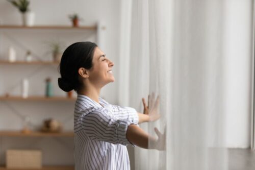 A woman opens some curtains.